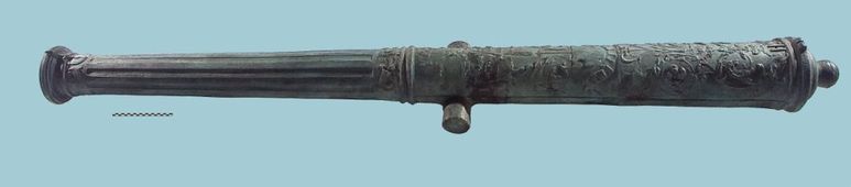 Bronzen kanonloop, een zogenaamde falcon. Het stuk werd gevonden in het scheepswrak in de Westerschelde bij Ritthem. Het betreft een voorlader, gemonteerd op een houten rolpaard, wellicht gegoten te Mechelen tussen 1520 en 1544, looplengte 230 cm.