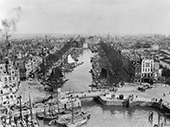 Gezicht op het Haringvliet in Rotterdam, circa 1900. Omstreeks de eeuwwisseling hadden alle havens in de stad een belangrijke functie voor de binnenvaart. Het grote aantal schepen in de haven geeft een duidelijk beeld hoe intensief het binnenvaartverkeer kon zijn. Op de voorgrond enige paard-en-wagens, die het aansluitend vervoer tussen de havens en de bedrijven in de stad verzorgden, terwijl op de kade een aantal vaten gereedligt voor verder vervoer. De foto is genomen vanaf het thans nog bestaande ‘Witte Huis’.