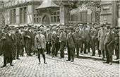 Nederlandse en Duitse schippers wachtend op lading en werk voor de schippersbeurs in Duisburg, circa  1920-1930. Hoewel verreweg het grootste deel van de Rijnvaart werd verzorgd door rederijen, was er in Duisburg een schippersbeurs waar particuliere schippers lading konden krijgen. Na de machtsovername door de nationaalsocialisten kregen de Nederlandse particuliere schippers in Duitsland die van de beurs gebruikmaakten het moeilijk. Hoewel de Akte van Mannheim dat uitdrukkelijk verbood, bevoordeelden de Nazi’s Duitse schippers, terwijl Nederlandse Rijnschippers die niet met de Nazi’s sympathiseerden bovendien aan allerlei intimidaties waren blootgesteld.