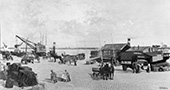 Stukgoederenoverslag bij Arnhem, 1929. Het vervoer van stukgoederen werd grotendeels verzorgd door de beurtvaart. Langs de kade zijn twee stoomboten afgemeerd om de goederen aan- en af te voeren. Bij het laden en lossen werd al van kleine hijskranen gebruikgemaakt. De aan- en afvoer over land geschiedde gedeeltelijk met vrachtauto’s, maar vaak ook nog met paard-en-wagens.