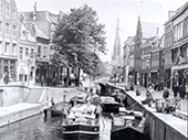 Marktschepen in Leeuwarden, circa 1910-1920. Op marktdagen trok een bonte vloot vaartuigen naar Leeuwarden om landbouwproducten en vee naar de markt te brengen. Vanwege de lage bruggen hebben de schippers hun masten gestreken en bomen ze hun vaartuigen voort. Het vervoer in de provincie Friesland was in deze periode nog kleinschalig.