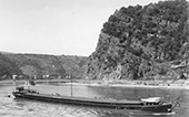 Rijnsleepschip <em>Saturnus</em> op sleep op de Duitse Rijn bij de bekende berg de Loreley, circa 1950. In de Rijnvaart gold de goede traditie dat bijna iedere reder de vaartuigen die hij aan zijn vloot toevoegde op deze karakteristieke locatie liet fotograferen. Tegenwoordig beschikken we daardoor over een groot aantal Loreley-scheepsfoto’s. De <em>Saturnus</em> voldeed aan de standaardafmetingen van een zogenaamd Rijn-Hernekanaalschip, met een lengte van 80 meter en een laadvermogen van 1.350 ton.