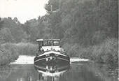 Vrachtschip <em>Vios</em> (circa 150 ton) op het Kanaal Deventer-Raalte, circa 1980. Het Kanaal Deventer-Raalte was het laatste nog voor de scheepvaart geopende deel van de Overijsselse kanalen en was toegankelijk voor kleine schepen met een laadvermogen tot 150 ton. Op de foto is duidelijk te zien hoe krap het kanaal voor de toenmalige binnenvaart was, een ontmoeting van twee van dergelijke vaartuigen was nauwelijks mogelijk. Door de sterke concurrentie van de vrachtwagen liep het binnenvaartvervoer op alle kleine vaarwegen tussen 1950 en 1970 sterk terug. Een aantal hiervan werd uiteindelijk voor de scheepvaart gesloten. Dit gold in 1988 na lange strijd ook voor het Kanaal Deventer-Raalte.