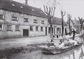 Voortgeboomde schuit op de Blekersvaart in Heemstede, omstreeks 1910. De Blekersvaart bevatte schoon kwelwater uit de duinen. Omdat het Haarlemse grachtwater sterk verontreinigd was, vestigden zich langs de vaart een aantal wasserijen, die van het schone duinwater gebruikmaakten. De gefotografeerde schuit heeft zojuist manden en tonnen met wasgoed van rijke gezinnen uit Haarlem naar Heemstede gebracht, of komt deze ophalen. Aan boord, de schipper die zijn vaartuig met een vaarboom voortbeweegt. Op de wal enkele medewerkers van de wasserij die helpen met laden of lossen. Vijftien jaar later was dit vervoer overgenomen door bestelwagens.