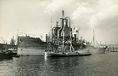 Graanoverslag vanuit het zeeschip Kossuth naar een sleepschip in de Waalhaven in Rotterdam, circa 1930. De overslag van graan vond plaats met zogenaamde elevatoren, grote drijvende werktuigen, die het graan in het ruim van zeeschepen opzogen en vervolgens via een pijp in een binnenschip stortten. De eerste kwam in 1896 in bedrijf. Daarvóór geschiedde de graanoverslag met menskracht. De inzet van deze werktuigen leverde een aanzienlijke besparing van arbeid en tijd en maakte de overslag veel goedkoper.