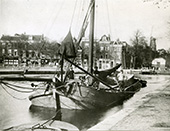 Afgemeerde geladen tjalk aan de Turfmarkt in Leiden, circa 1930. De schipper zit bij de mast, een jongen staat aan stuurboord in het gangboord. Schipperskinderen gingen vaak al op jeugdige leeftijd varen bij een familielid, om daar verdere ervaring op te doen.